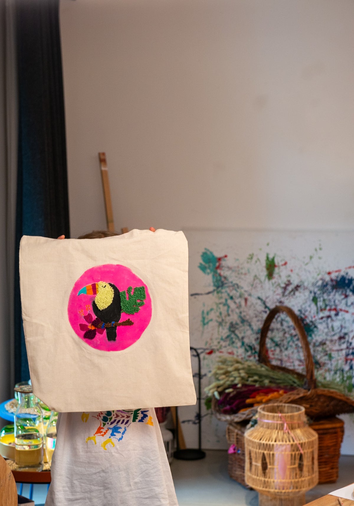 Eine Person hält ein buntes Tukan-Tuch für den kreativen Kindergeburtstag „Punch Needle & Jutebeutel“ von Straightcurls in der Hand.