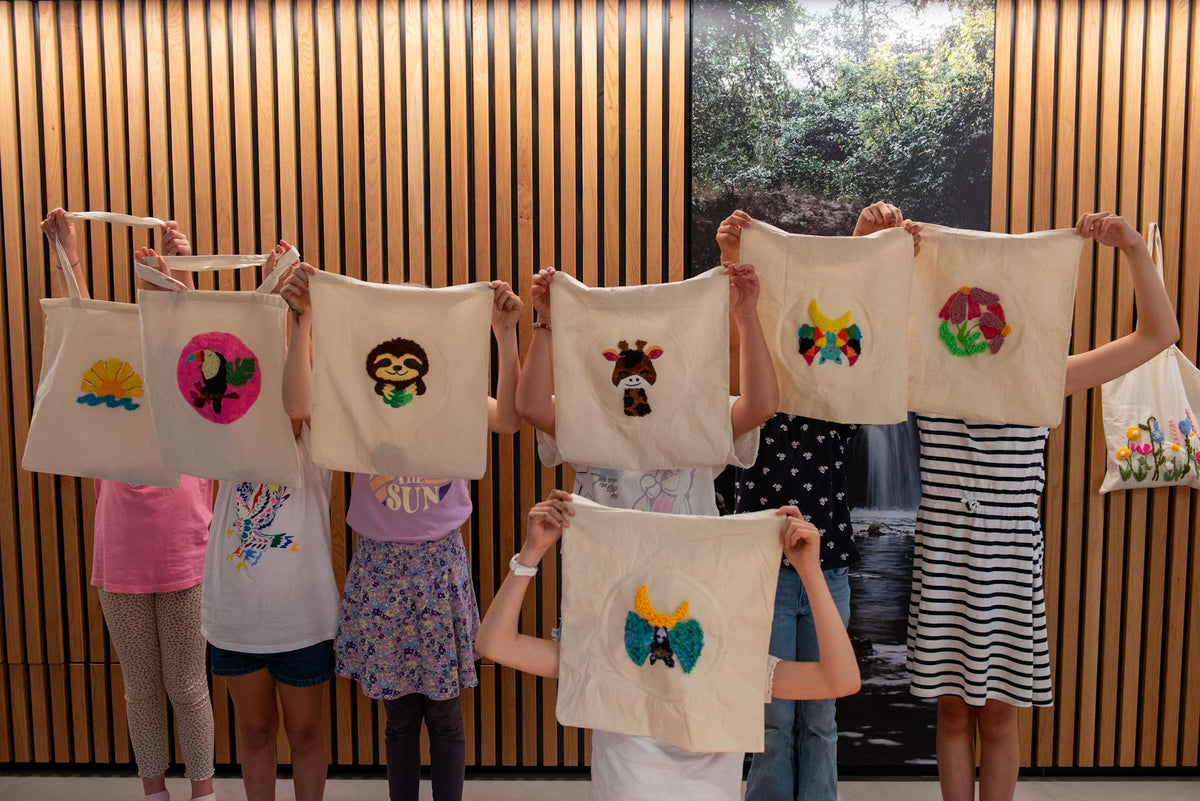 Sieben Kinder halten „Straightcurls Punch Needle & Acryl“-Jutetaschen hoch – ein kreativer Kindergeburtstag in Emmering, die Gesichter sind verdeckt.