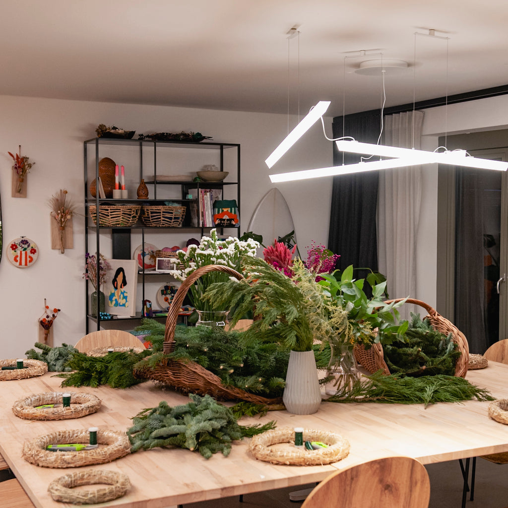Ein gedeckter Tisch für einen StraightCurls-Adventskranz-Workshop bei FFB Emmering mit Tannengrün und Körben in einem hellen Atelier.