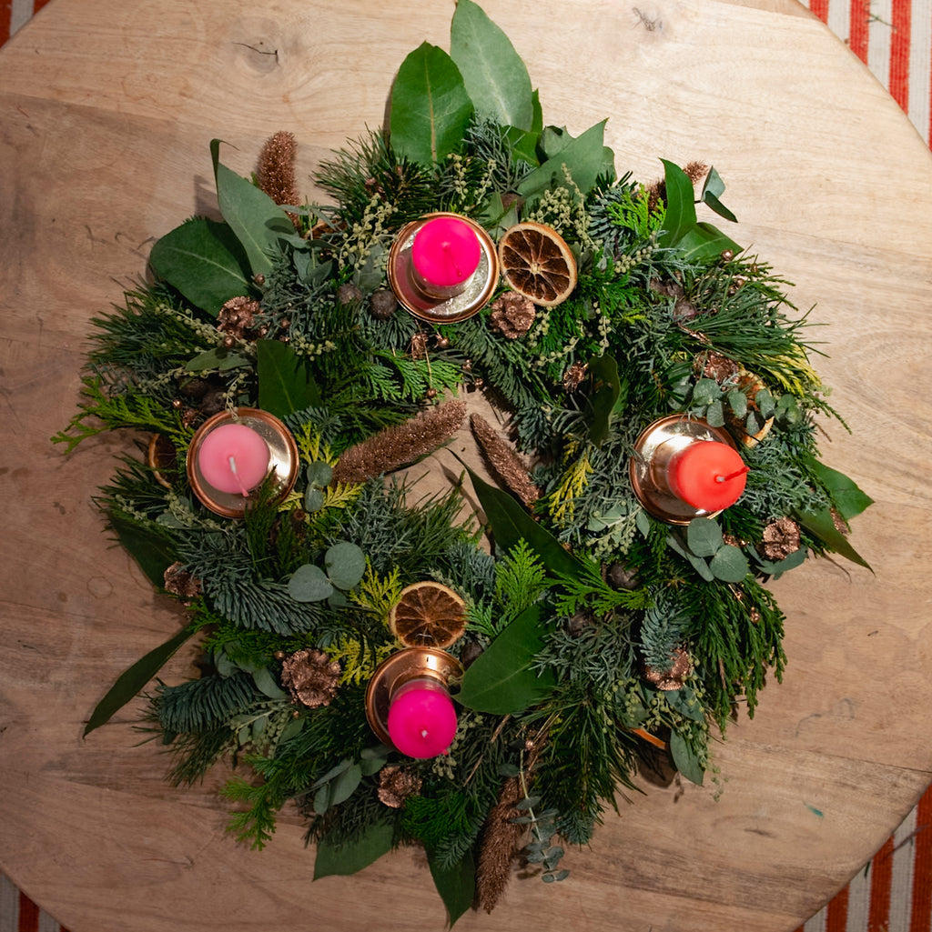 StraightCurls’ Adventskranz-Workshop FFB Emmering: grüner Kranz, 4 rosa Kerzen, Orangenscheiben, Tannenzapfen auf Holz.