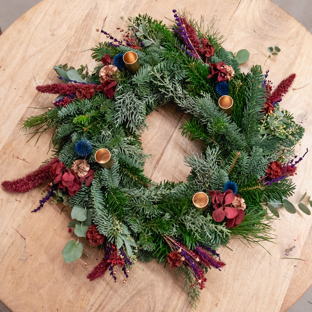 Ein StraightCurls-Adventskranz-Workshop bei FFB Emmering mit bunten Blumen und goldenen Haltern auf einem Holztisch.