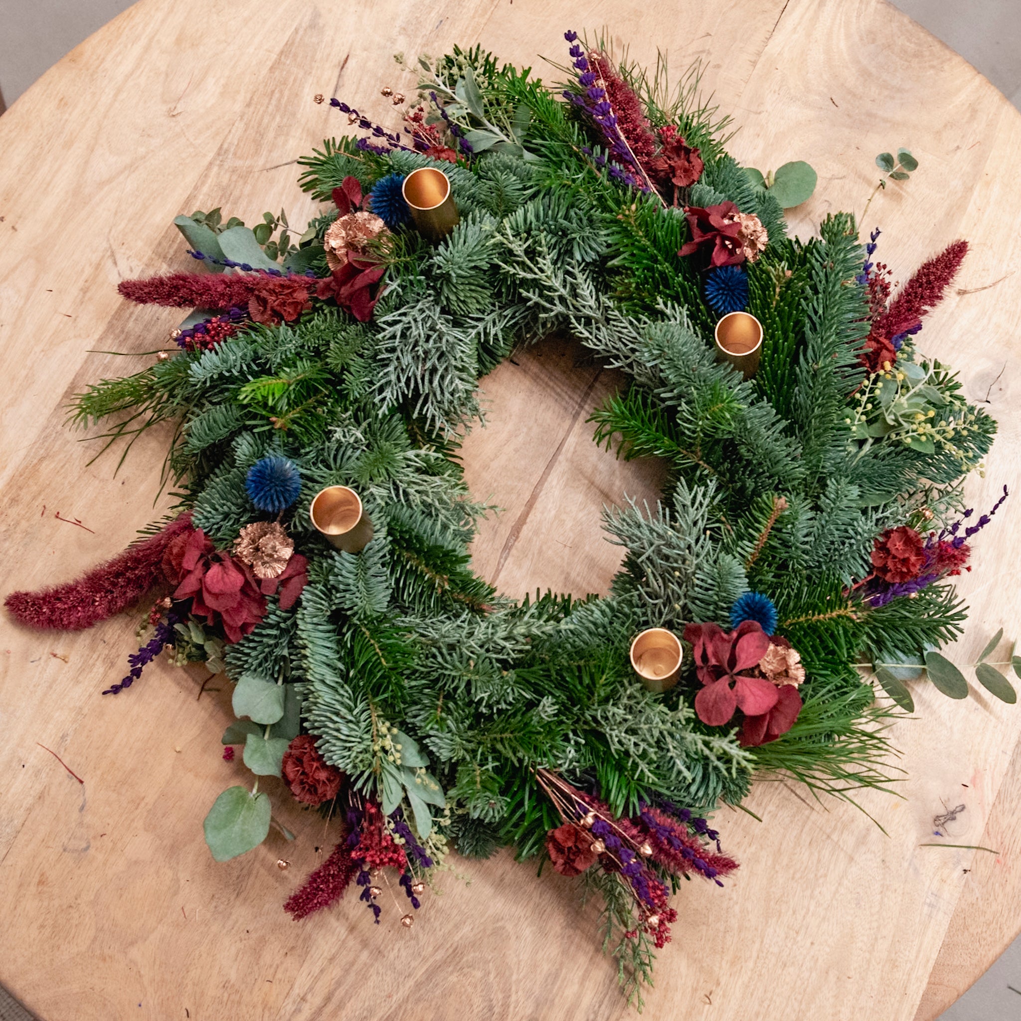 Ein StraightCurls-Adventskranz-Workshop bei FFB Emmering mit bunten Blumen und goldenen Haltern auf einem Holztisch.