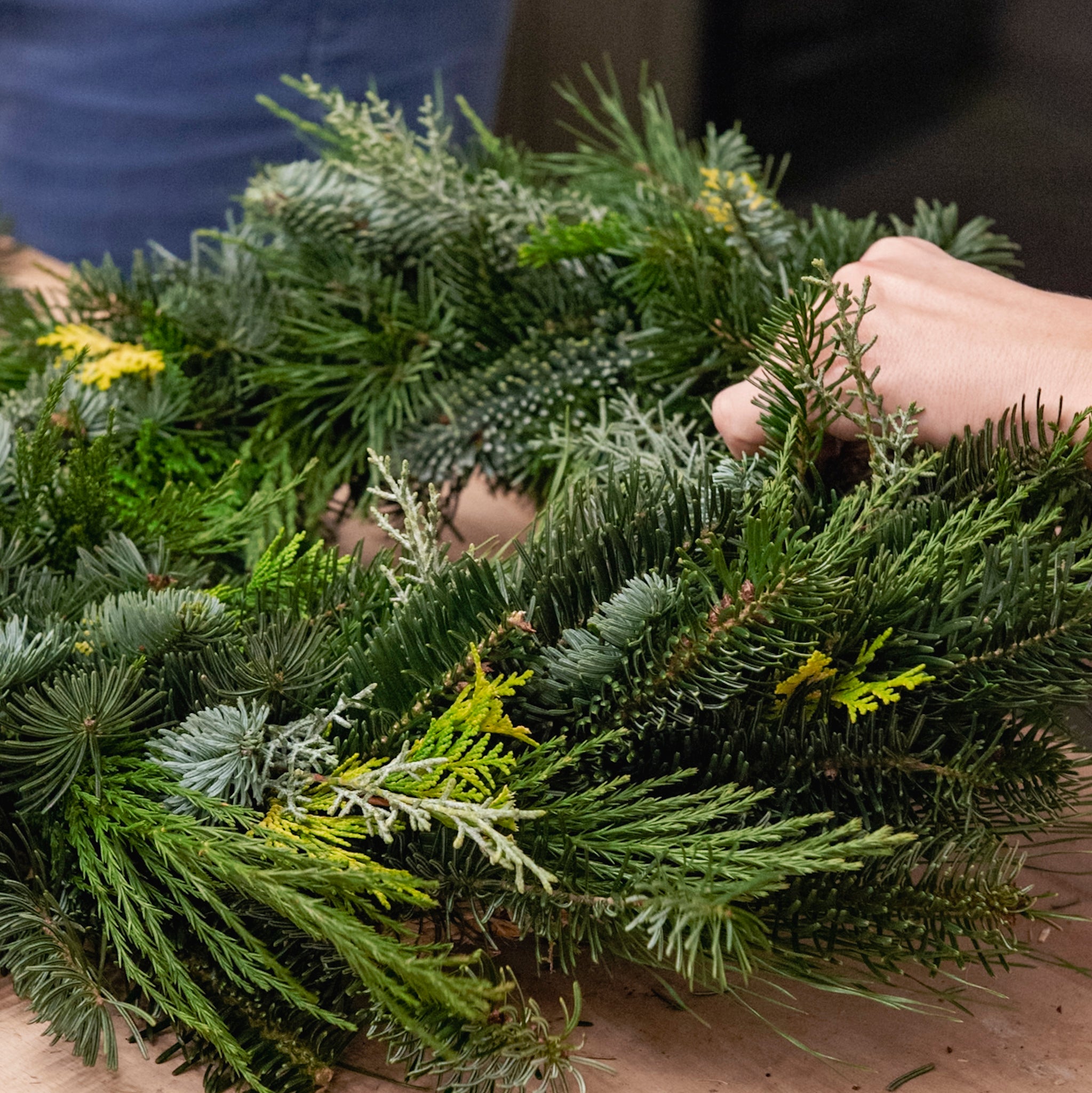Eine Hand formt im Rahmen des Adventskranz-Workshops „FFB Emmering“ von StraightCurls auf einer Holzunterlage einen Kranz.
