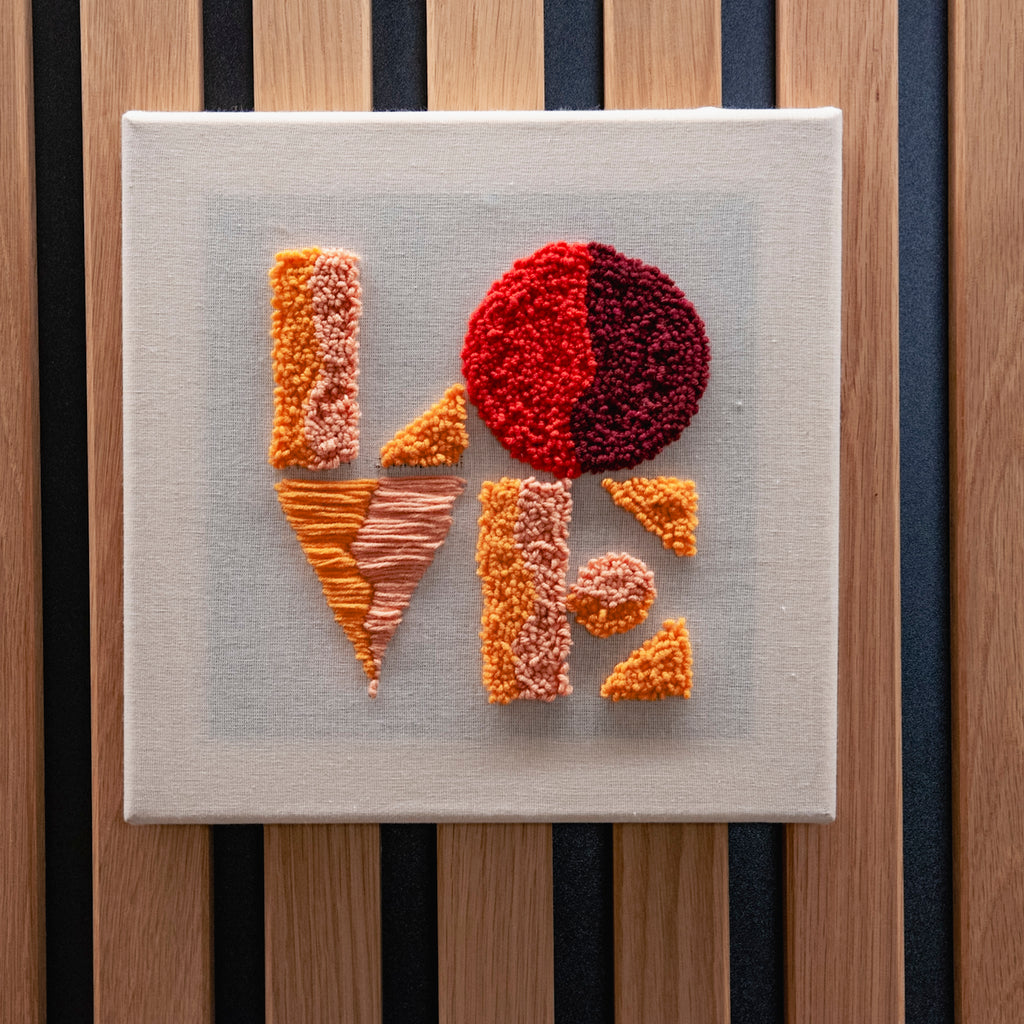 Der „Straightcurls Punch Needle Keilrahmen“ im Format 24 x 24 cm zeigt das Wort „LOVE“ in geometrischen Mustern auf einer handgespannten Leinwand.