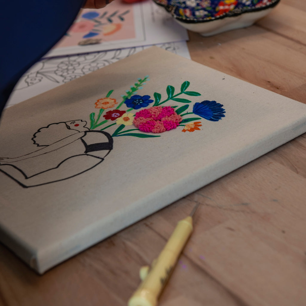 „Straightcurls Punch Needle Keilrahmen 24 x 30 cm“ zeigt eine unvollständige Figur mit bunten Blumen und Malutensilien.
