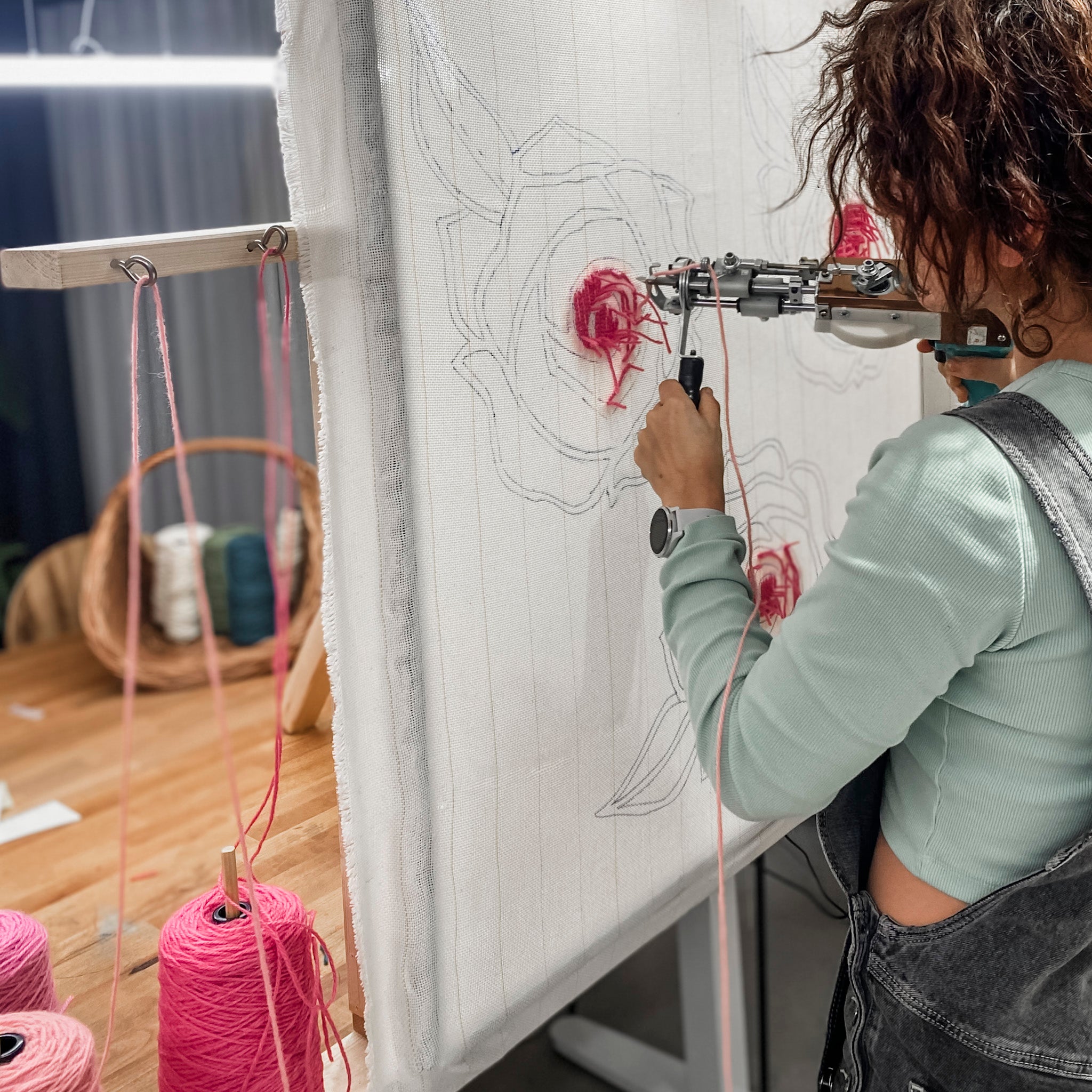 Person im Tufting-Workshop FFB Emmering by StraightCurls bei der Herstellung eines Rosenmusters, rosa Garnspulen auf dem Tisch.