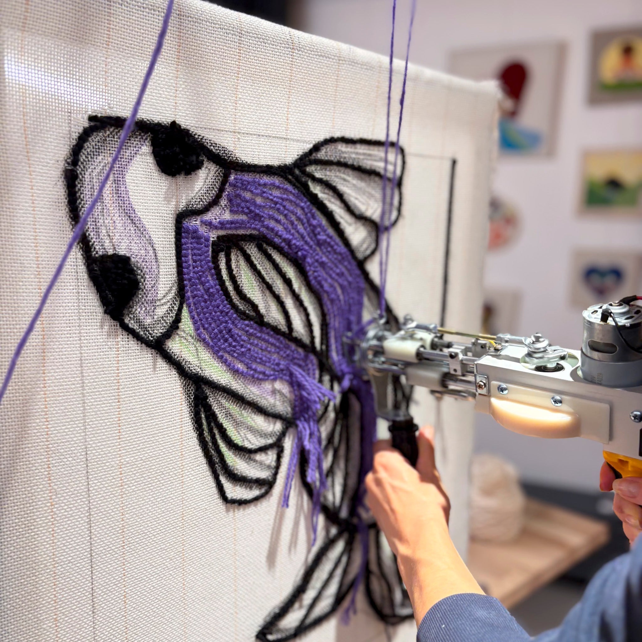 Jemand benutzt den Tufting Workshop FFB Emmering von StraightCurls, um einen lila Fisch auf einem Teppichkunstwerk zu tuften.
