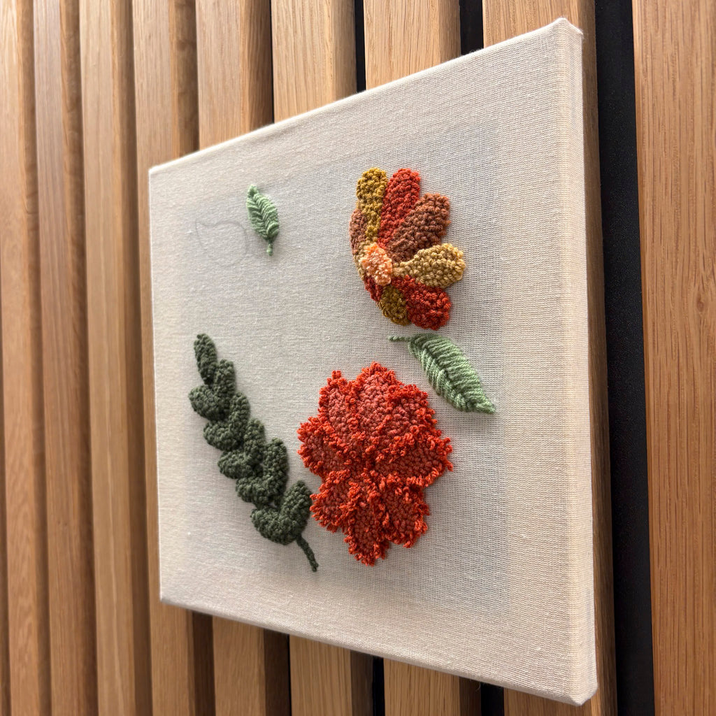 Eine Punch Needle Workshop FFB Emmering Leinwand von StraightCurls mit orange/roten Blumen und grünen Blättern auf Holzlatten.