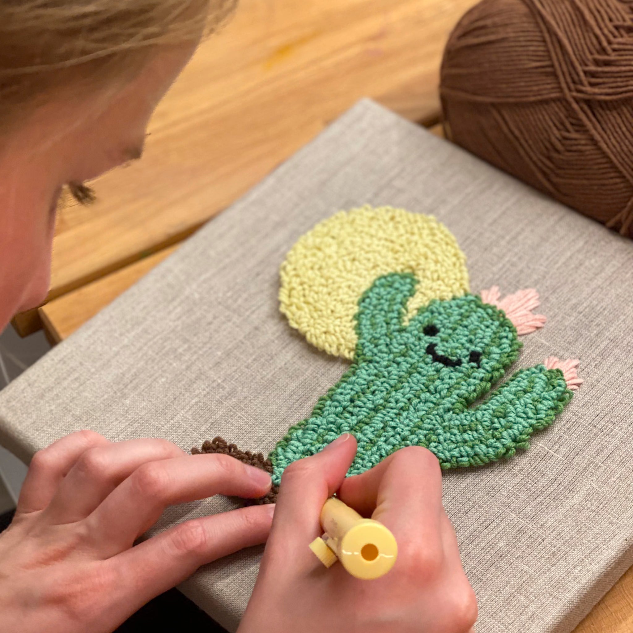 Ein gepunchter grüner Kaktus mit Gesicht in einem Stickrahmen, der während des Punch-Needle-Prozesses detailreich ausgearbeitet wird.