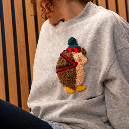 Detailansicht eines textilen Igel-Aufnähers auf einem Sweatshirt, der die plastische Schlaufenstruktur einer Stanznadel zeigt.