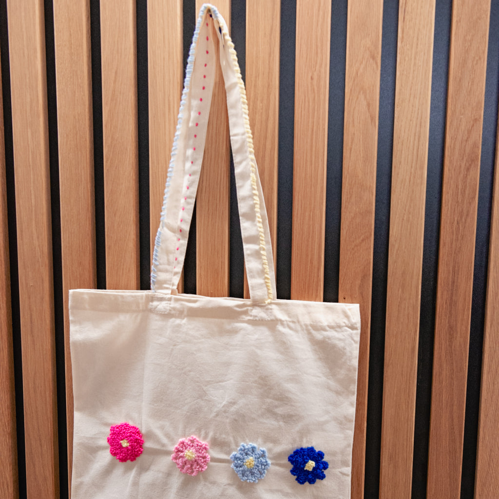 Cremefarbene Tragetasche mit vier gehäkelten Blumen von StraightCurls, hergestellt im Punch-Needle-Jutebeutel-Workshop des TIM Augsburg.