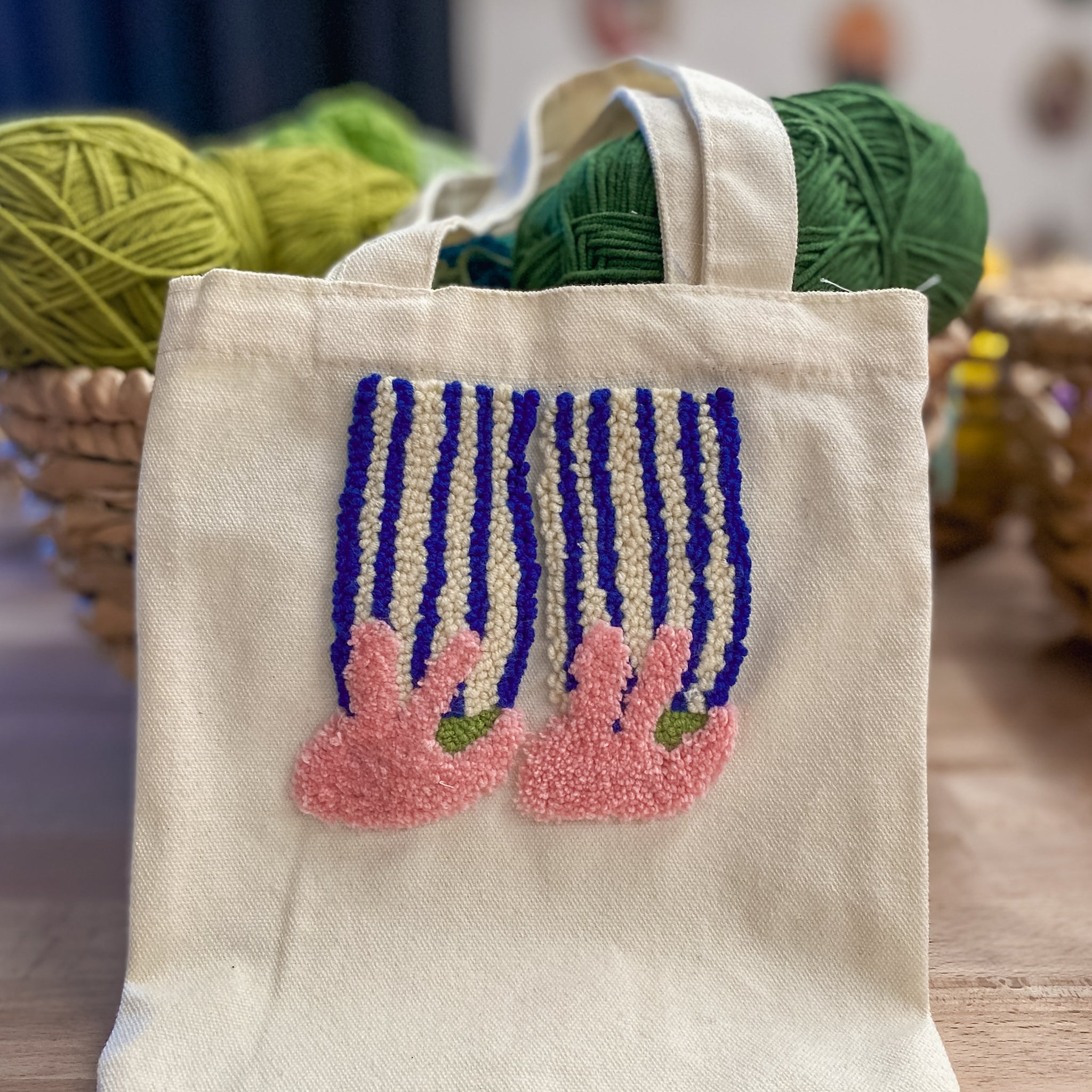 „StraightCurls Punch Needle Jutebeutel“ von Workshop TIM Augsburg, cremefarbene Tragetasche mit rosa und blauer Stickerei.