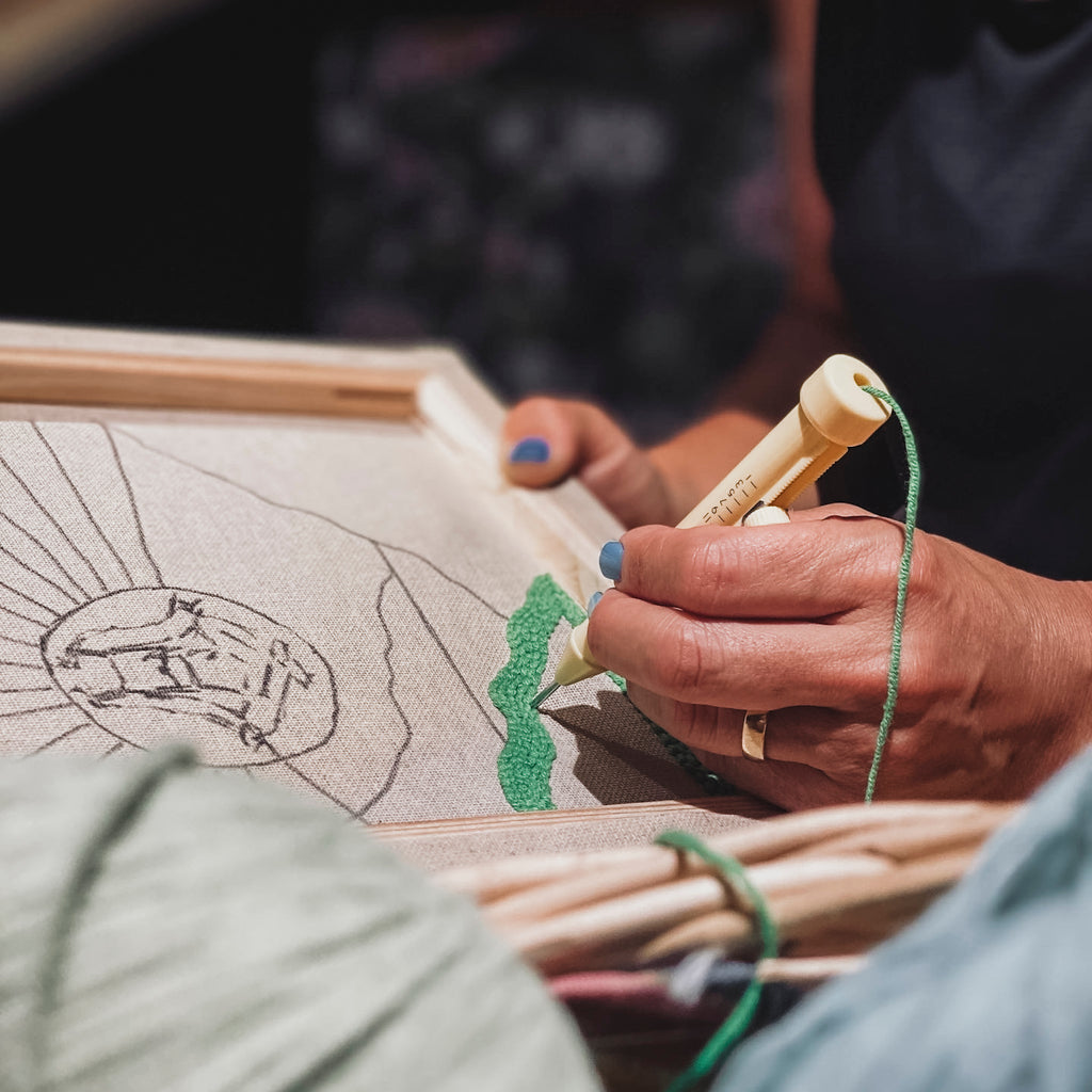 Detailaufnahme einer Hand, die eine verstellbare Punch Needle präzise entlang einer vorgezeichneten Linie auf hellem Stoff führt.
