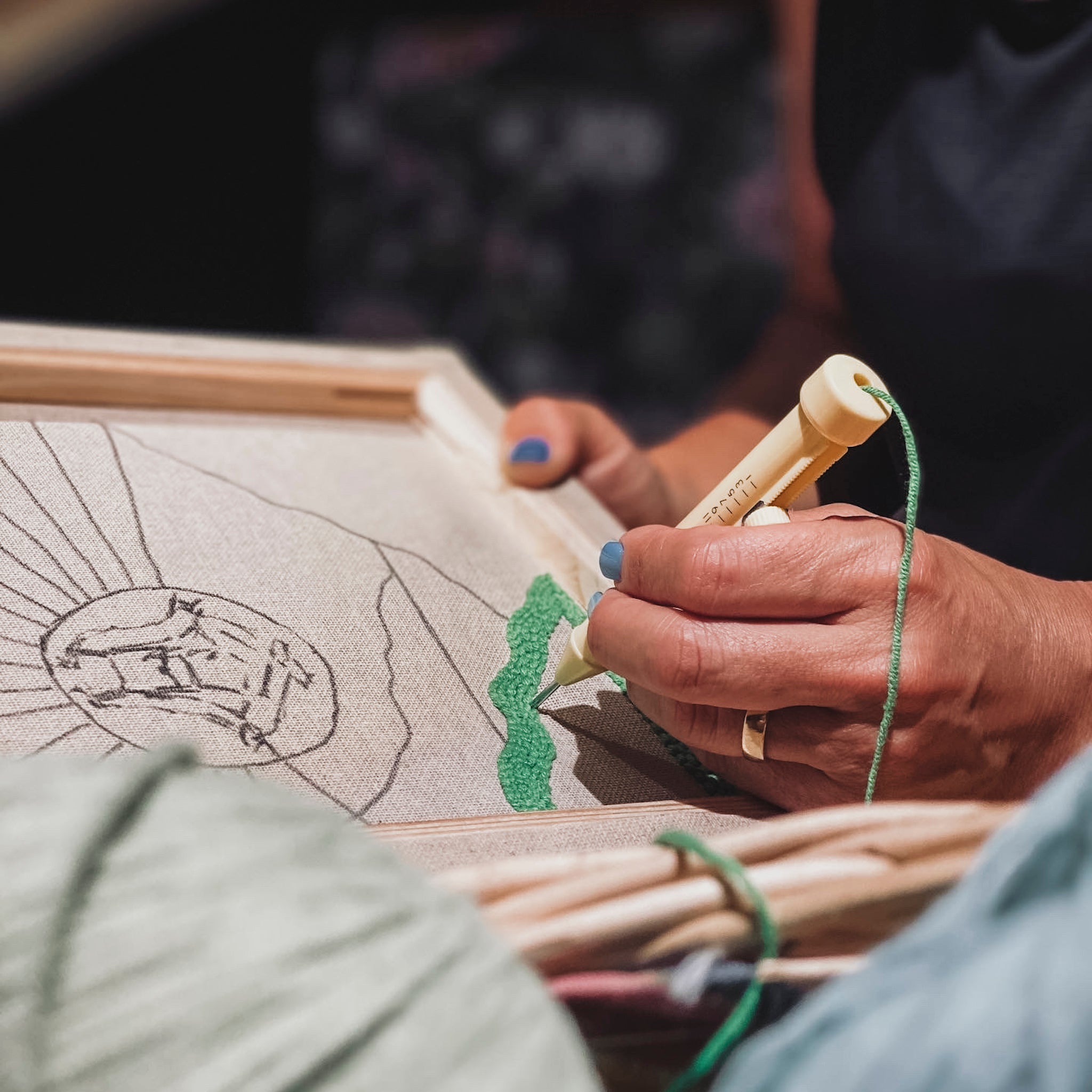 Detailaufnahme einer Hand, die eine verstellbare Punch Needle präzise entlang einer vorgezeichneten Linie auf hellem Stoff führt.