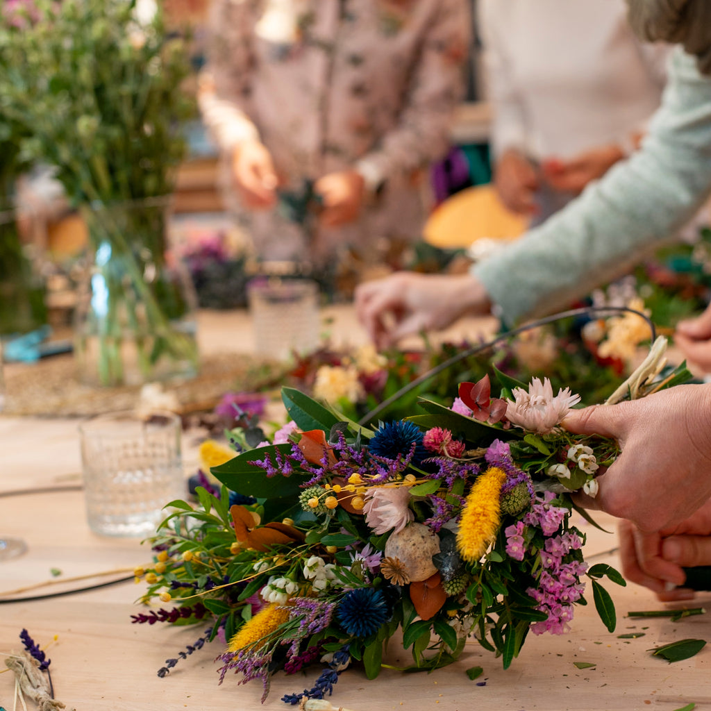 Fokus auf die präzise Handarbeit beim Binden eines farbenfrohen Kranzes im StraightCurls Workshop.