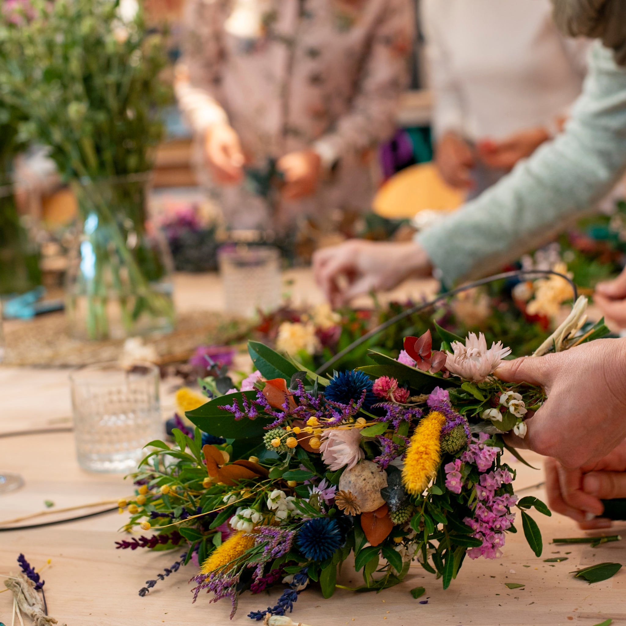 Fokus auf die präzise Handarbeit beim Binden eines farbenfrohen Kranzes im StraightCurls Workshop.