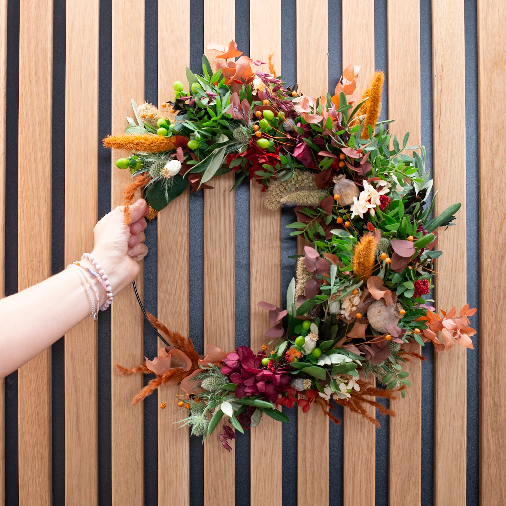 Eine Hand hält einen langlebigen herbstlichen Blumenkranz mit Beeren und frischen Zweigen von StraightCurls.