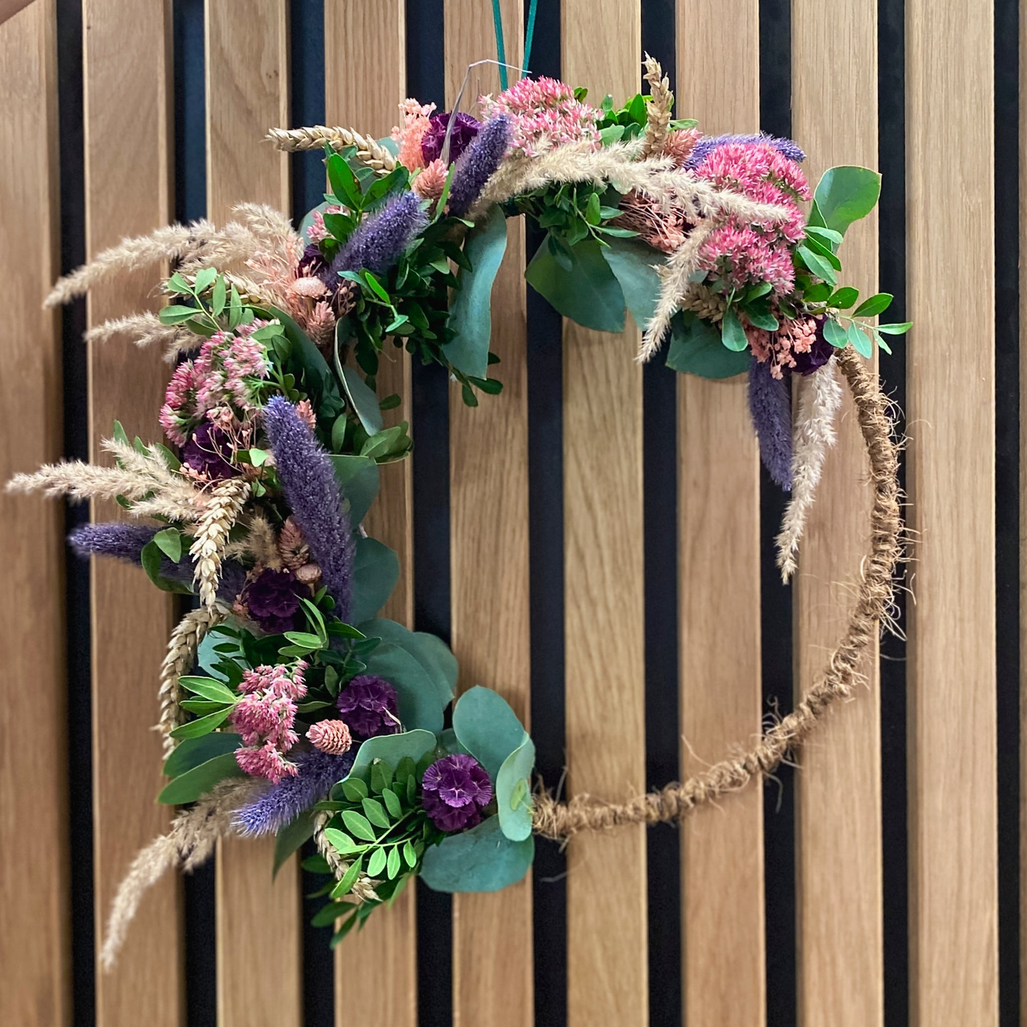 Haptischer Blumenkranz auf juteumwickeltem Rahmen mit lila und pinken Blüten von StraightCurls.