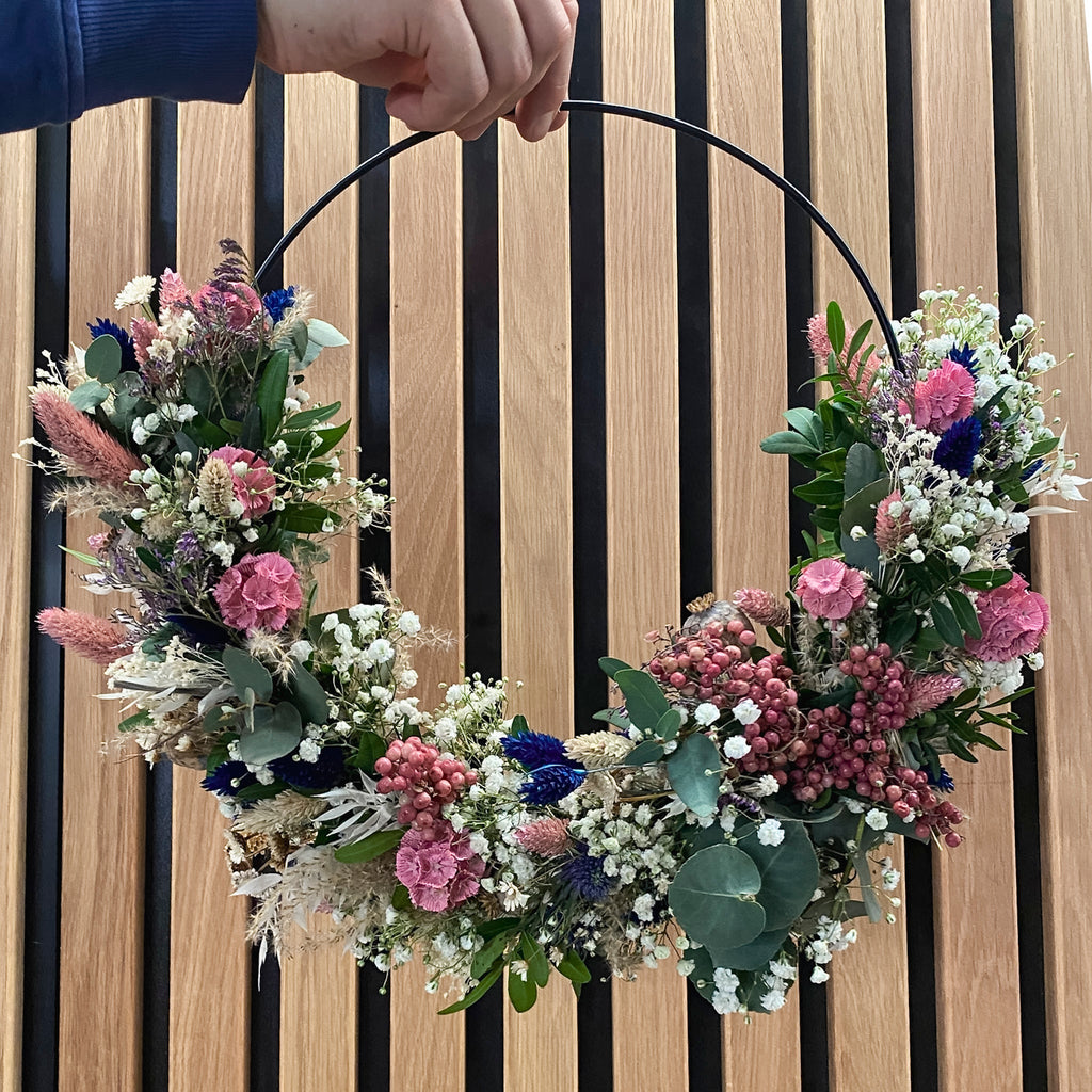 Moderner Blumenkranz auf einem schwarzen Metallring mit pinken und blauen Akzenten von StraightCurls.