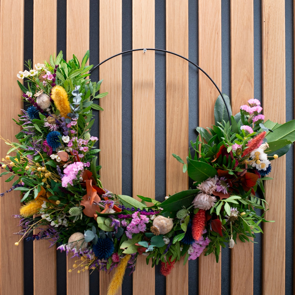 Moderner Blumenkranz auf schwarzem Metallring mit gelben und blauen Akzenten von StraightCurls.