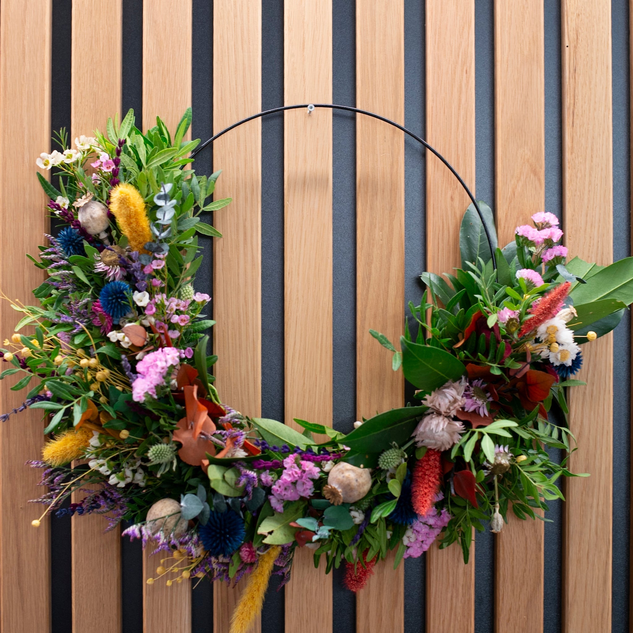 Moderner Blumenkranz auf schwarzem Metallring mit gelben und blauen Akzenten von StraightCurls.