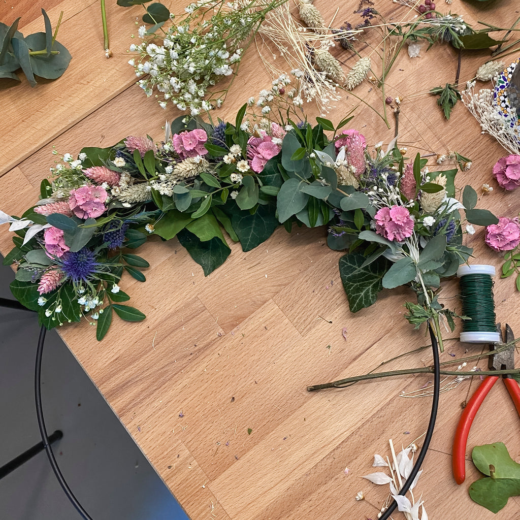 Ein neuer Blumenkranz auf schwarzem Metallring im Entstehungsstadium bei StraightCurls.