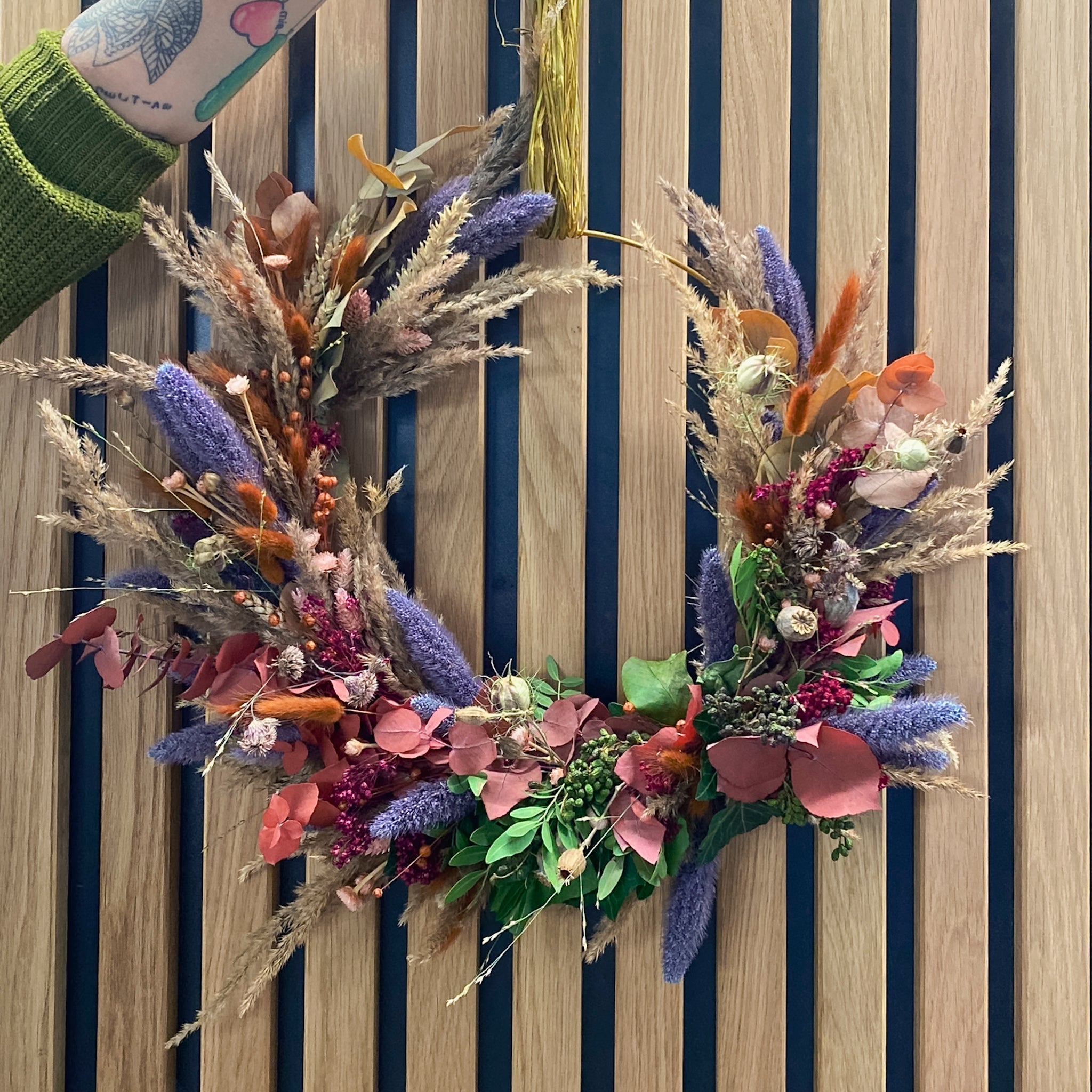 Voluminöser Kranz aus getrockneten Gräsern und lila Blütenelementen von StraightCurls.