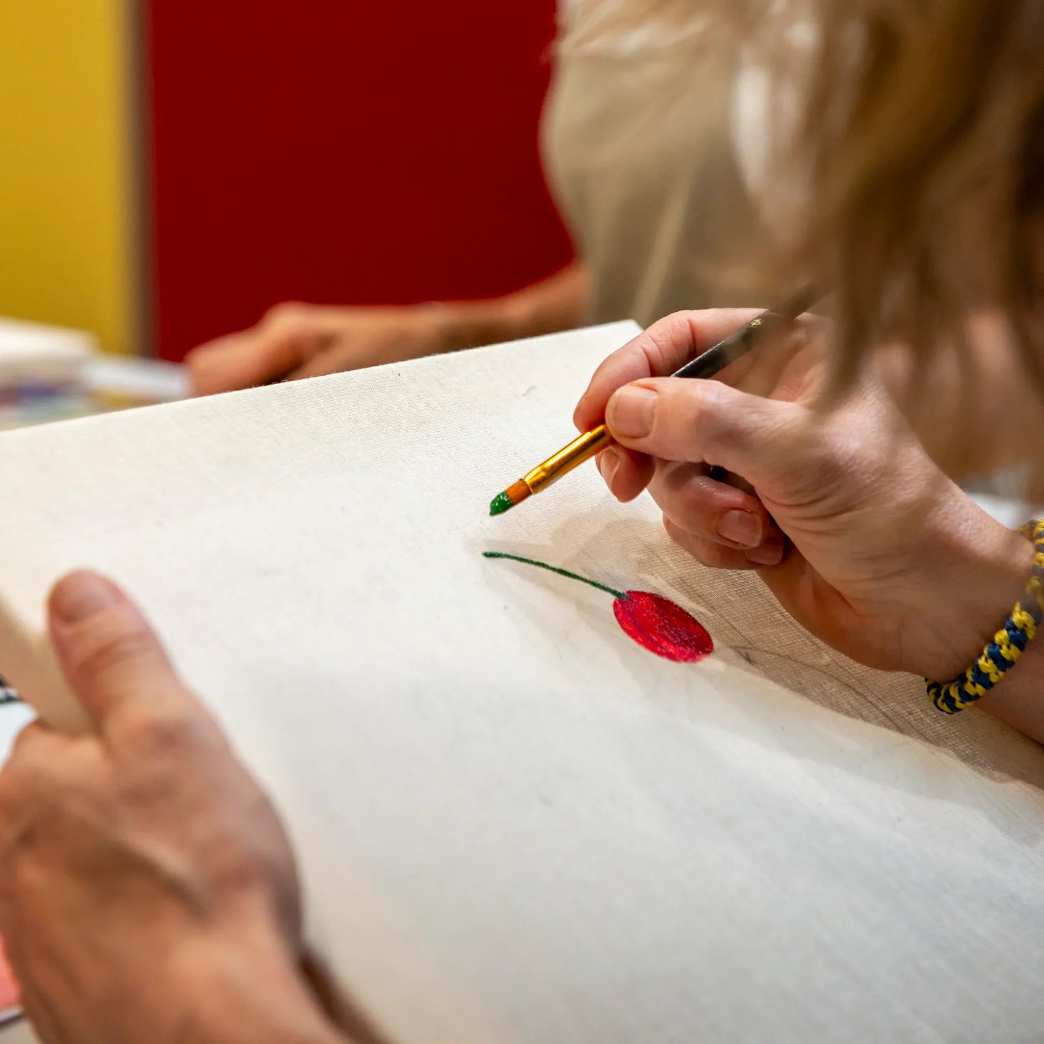 Eine Person malt eine rote Kirsche auf Leinwand beim StraightCurls Punch Needle meets Acryl Workshop FFB Emmering.