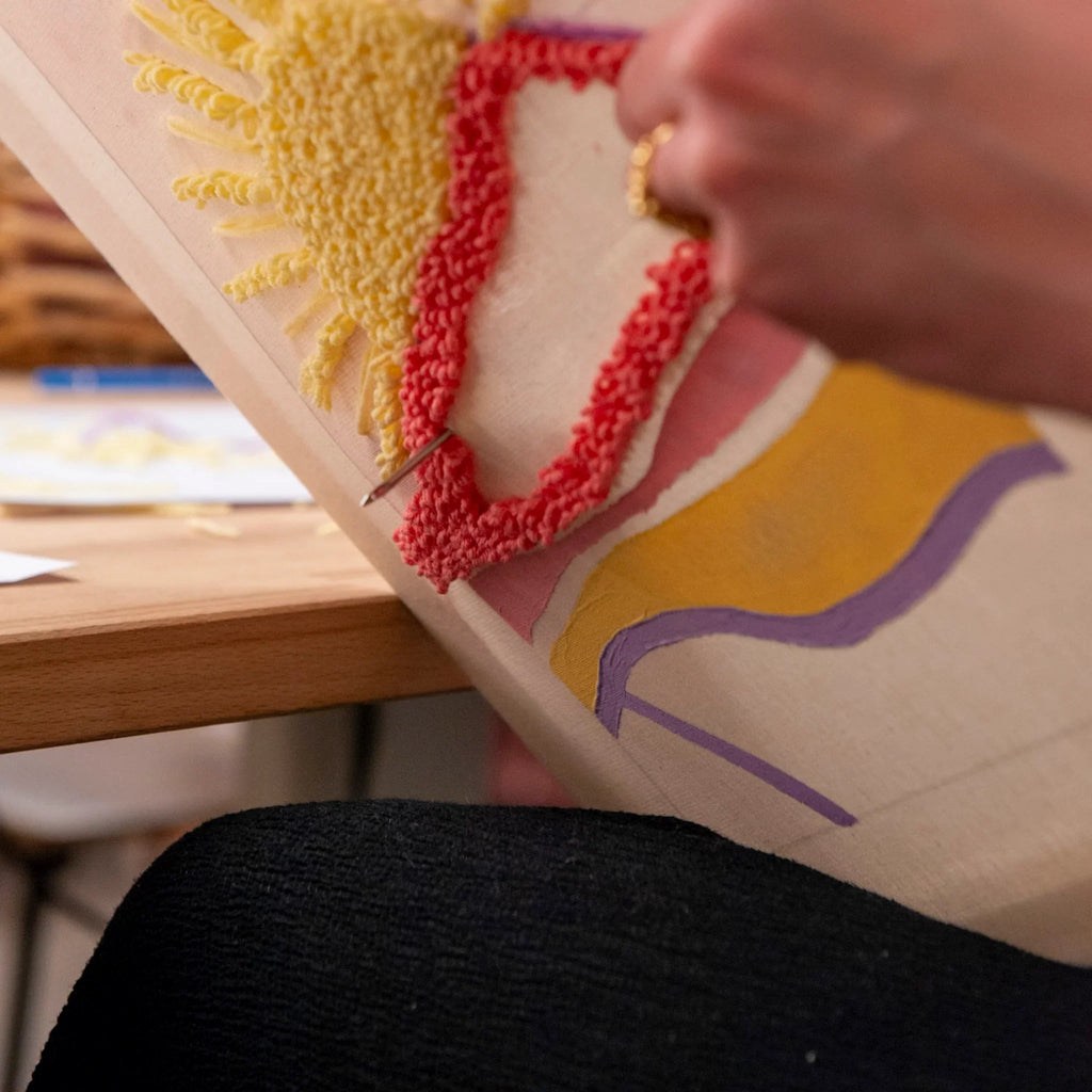 Eine Person benutzt StraightCurls Punch Needle meets Acryl Workshop FFB Emmering, um bunte Textilien auf Stoff zu gestalten.