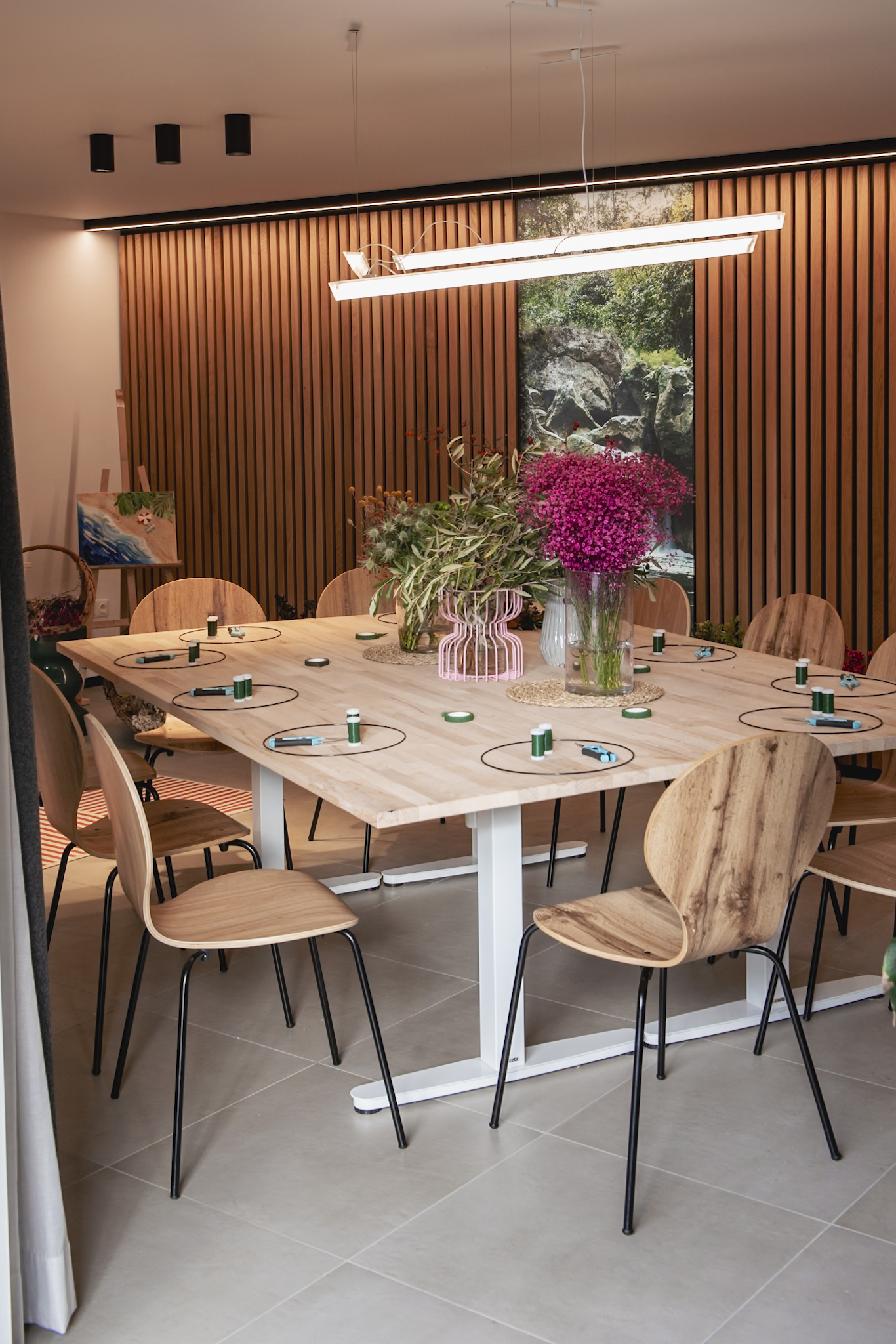 Impressionen aus dem Blumenkranz-Workshop im StraightCurls Atelier in Fürstenfeldbruck Emmering: Teilnehmerinnen binden an hellen Holztischen herbstliche Kränze aus frischen Blumen und Trockenblumen um einen Metallring. Man sieht Scheren, Draht und eine große Auswahl an Naturmaterialien in einer gemütlichen Workshop-Atmosphäre.